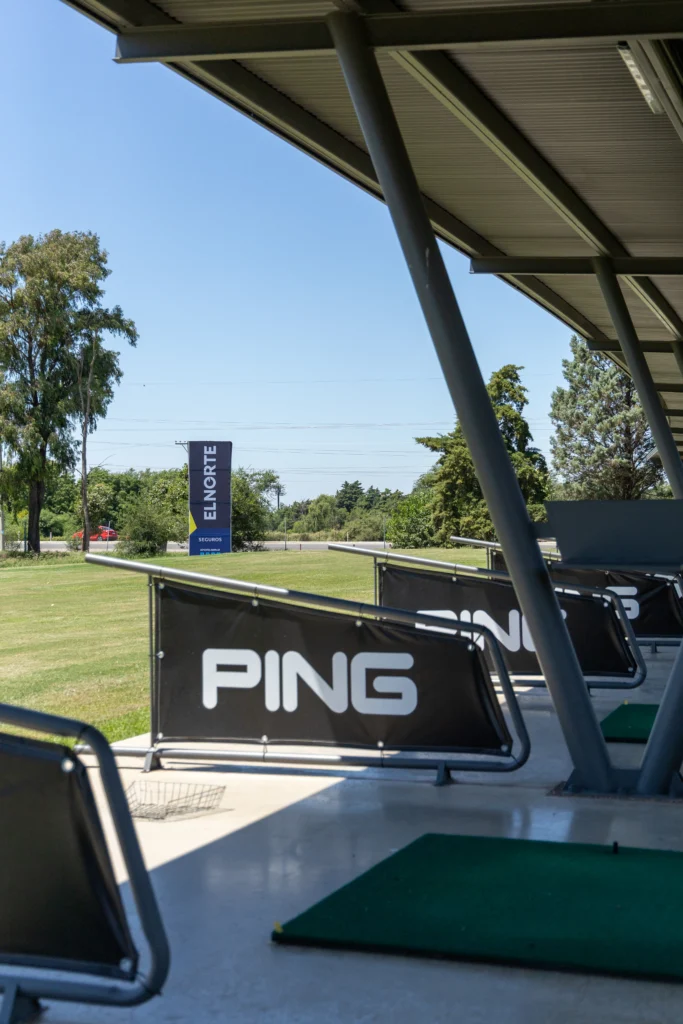 Un tee individual con el cartel de PING y la cancha de práctica hacia afuera.